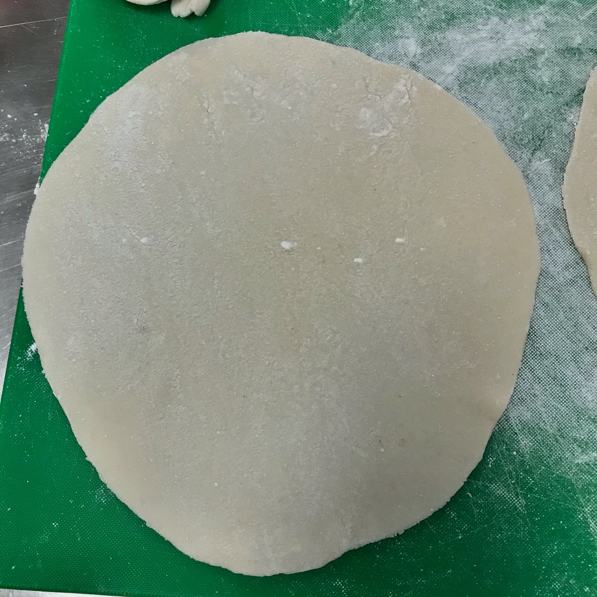 image show a circle of gluten free dough on a green cutting board