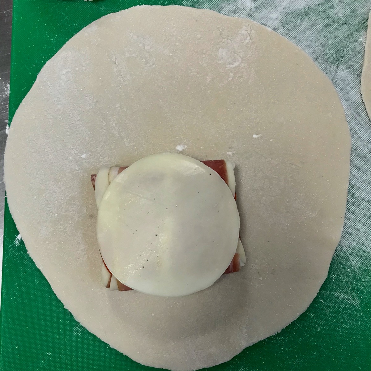 image of a gluten free pizza dough circle with 4 slices of lunch meat and 6 slices of cheese rolled up to be encased in the dough to form a calzone